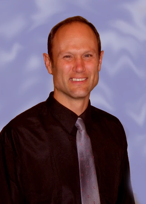Dr. Ron Engler wearing a collared shirt and tie, sitting for a professional photo